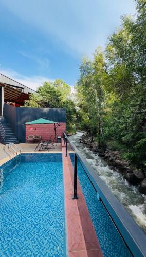 a swimming pool next to a river next to a house at Пар&Речка in Almaty