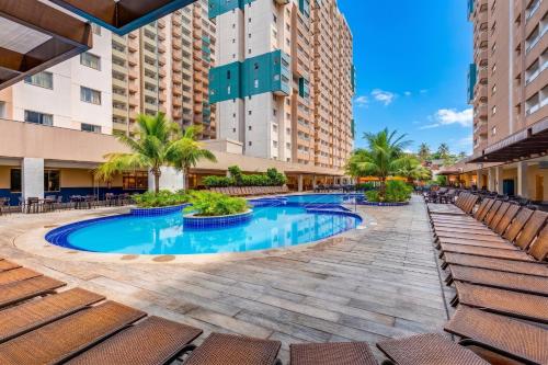 a resort pool with chairs and palm trees and buildings at Enjoy Olímpia Park Resort in Olímpia