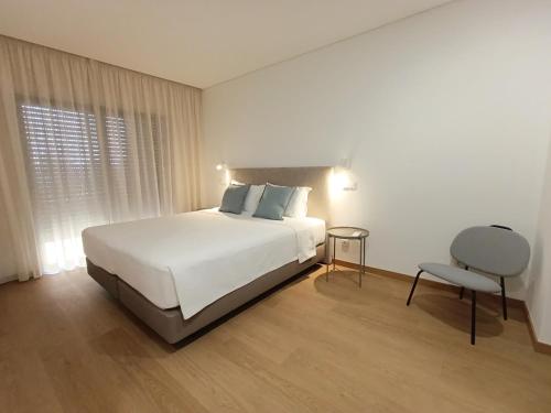a bedroom with a white bed and a chair at Entrecubos Apartamentos in Olhão