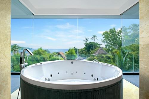 a bath tub in a room with a large window at Le Meridien Bali Jimbaran in Jimbaran