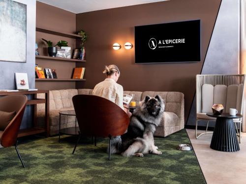 a man sitting at a table with a dog sitting on a chair at Novotel Grenoble Centre in Grenoble