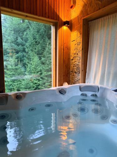 a bath tub in a room with a window at Oskarówka domek w górach na odludziu z jacuzzi i sauną - kominek i Netflix in Szczawa