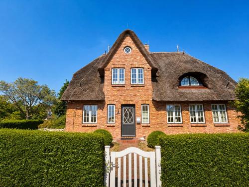 a house with a thatched roof with a white fence at Haus "Carla Marie" in Hedehusum
