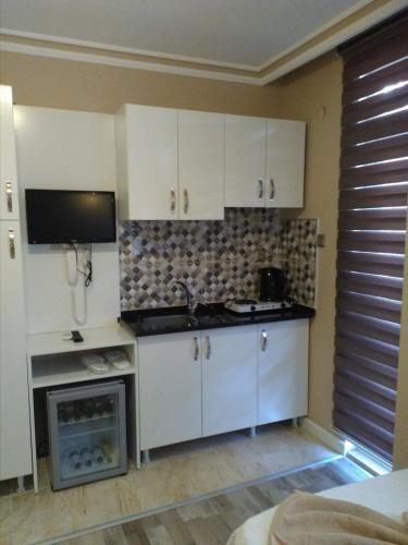 a kitchen with white cabinets and a tv on the wall at Send Apart Otel in Antalya