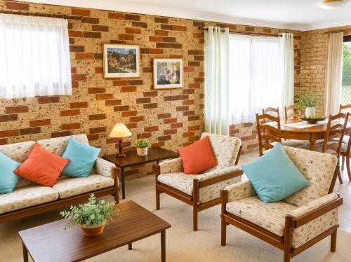 a living room with couches and chairs and a brick wall at Seascape Carroll Avenue - close to Mollymook Beach in Mollymook