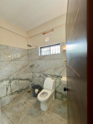 a bathroom with a toilet and a window and a door at Fruits Garden Resort in Kotamangalam