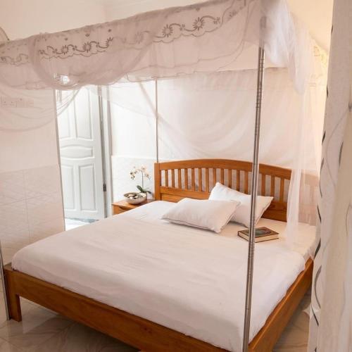 a bedroom with a canopy bed with white sheets at Delhi Gardens Hotel in Fort Portal