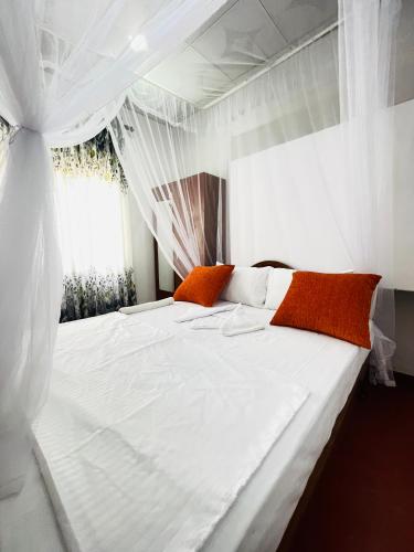 a white bed with orange pillows in a bedroom at Villa Dinusara in Weligama