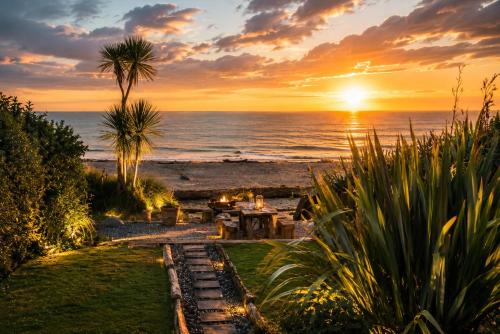 a sunset over the ocean with a table and a grill at Drifting Sands Beachfront Retreat in Hokitika