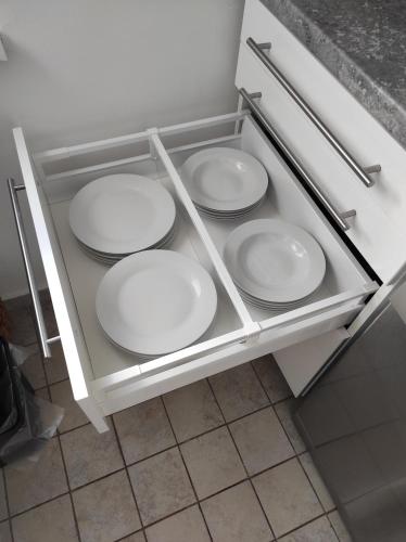 four white plates in a drawer in a kitchen at Apartman Garami Porta in Mezőkövesd