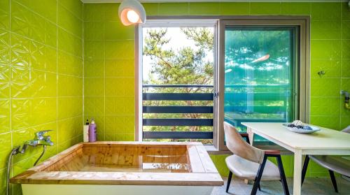 a tub in a green bathroom with a table and a window at Yeongheungdo J Pension in Incheon
