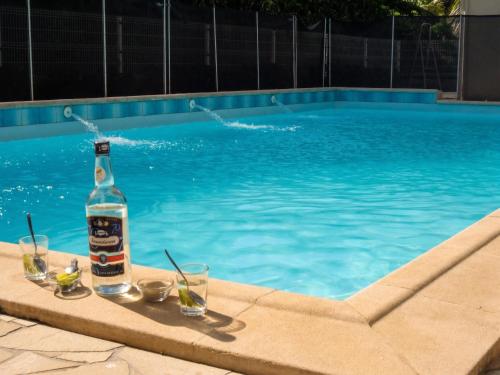 a bottle of beer and glasses sitting next to a swimming pool at Studio charmant à Sainte-Anne, 23 m², piscine partagée in Sainte-Anne