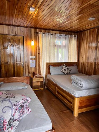 two beds in a room with wooden walls and wooden floors at Chyajalo homestay in Darjeeling