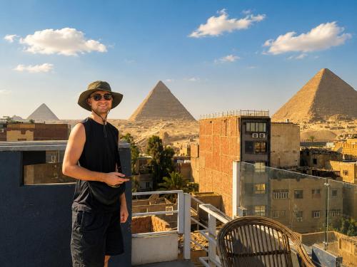 a man standing on a balcony with pyramids in the background at Prince Pyramid HoteLL in Cairo