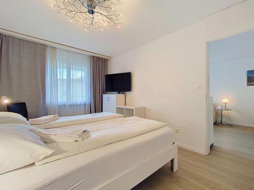 a white bedroom with two beds and a television at Apartment Allod Park Haus B 202 by Interhome in Davos