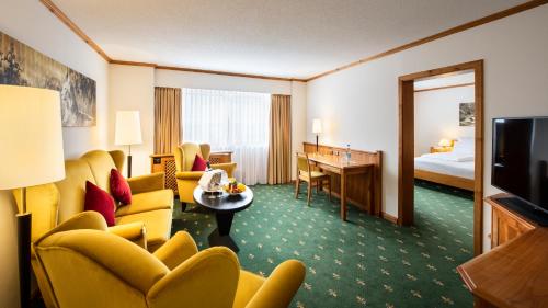 a hotel room with yellow chairs and a room with a bed at Sonnenhof Resort Himmelreich Bayerischer Wald in Lam