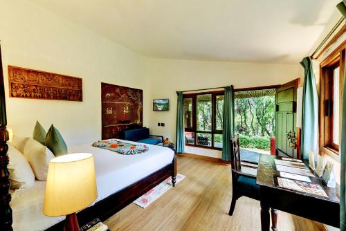 a bedroom with a bed and a desk and a window at Indo Asia Heritage Coorg, formerly Heritage Resort Coorg in Madikeri