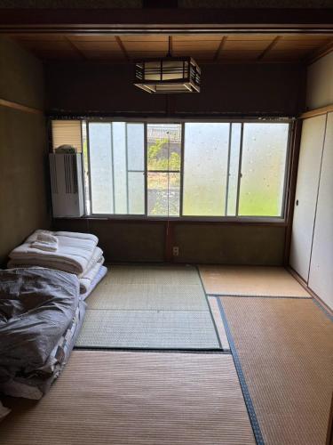 an empty room with a bed and two windows at ゲストハウス奥白浜 in Shirahama