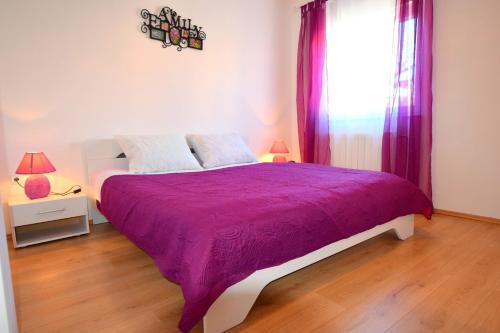 a bedroom with a bed with a purple comforter and a window at Apartments Celebrini in Malinska