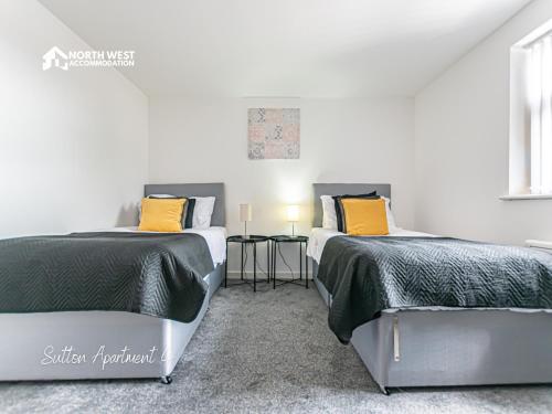 two beds in a room with white walls and yellow pillows at Modern Serviced Apartments in St Helens with Free WiFi Ideal for Leisure or Work Stays by North West Accommodation in Saint Helens