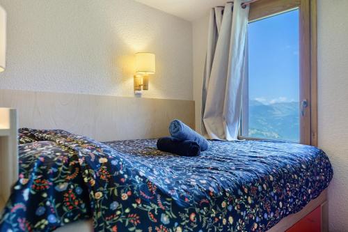 a bedroom with a bed with a blue blanket and a window at Grand studio Cosy divisible in Valmorel