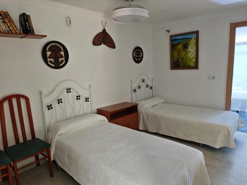 a bedroom with two beds and a chair and a butterfly on the wall at En Resort Fincas Las Dunas dos Chalets con jacuzzis en primera linea de playa , uno de 4 dormitorios y otro de 2 dormitorios, Llama al Seiscientos veintisiete Cuatrocientos diecisiete Trescientos noventa y ocho in Rota