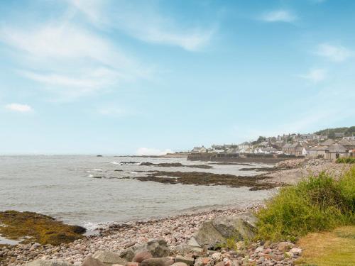 a rocky beach with houses and the ocean at Fifie Cottage in Johnshaven