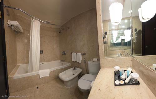 a bathroom with a tub and a toilet and a sink at Golden Tulip Bahrain in Manama