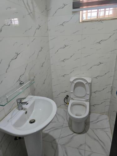 a white bathroom with a toilet and a sink at O2 Continental Suites in Kubwa
