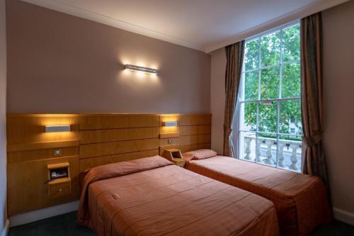 two beds in a hotel room with a window at The Nayland Hotel in London