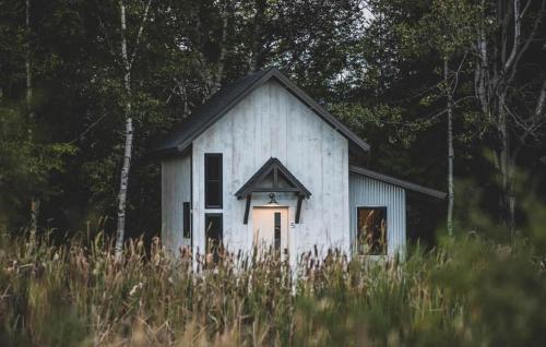 a small white house in a field of tall grass at The Alpine Suite | Walk to Downtown & Rangeley Lake Beach in Rangeley