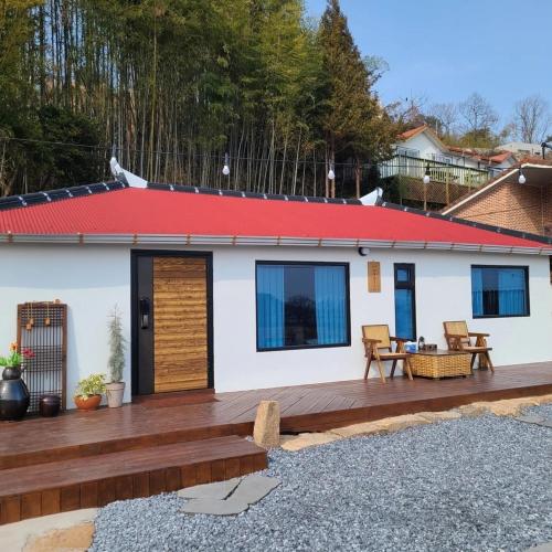 a house with a wooden deck with a red roof at Namhae Choncangs in Namhae