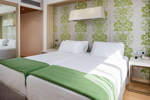 a bedroom with a large white bed with green sheets at NH Ciudad Real in Ciudad Real