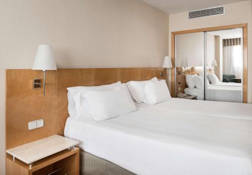 a bedroom with a large white bed and a mirror at NH Ciudad Real in Ciudad Real