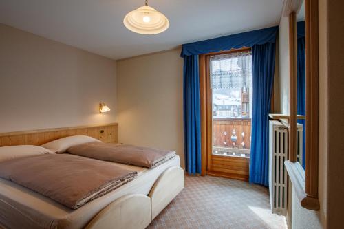 a bedroom with a bed and a window with blue curtains at Albergo Caravasc in Livigno
