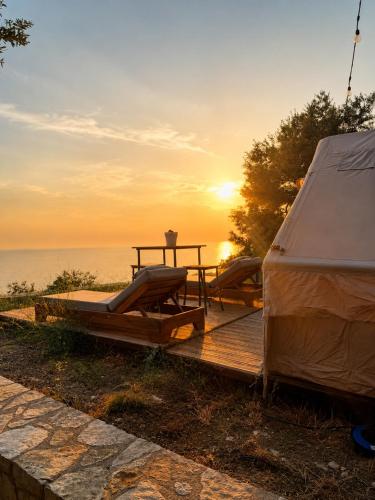 a tent and a table on a wooden deck with the sunset at Cimarte The Path Lukove in Lukovë