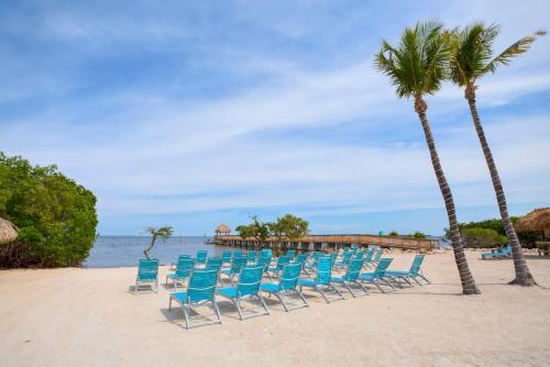 a row of chairs and palm trees on a beach at Keys Waterfront Condo with Beach Pool Sunset Views in Tavernier