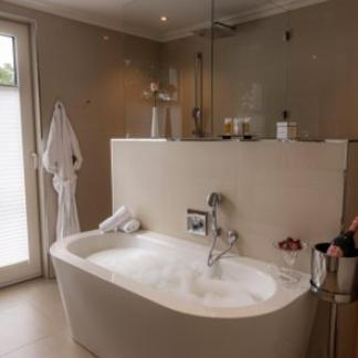 a bathroom with a large white tub with a mirror at Strandhotel Fontana in Timmendorfer Strand