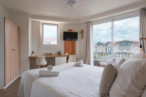 a bedroom with a white bed with a large window at Hôtel La Baïne in Capbreton