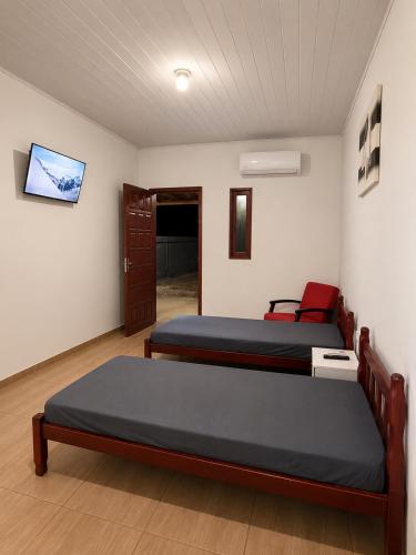a bedroom with two beds and a tv on the wall at Pousada Vale das Flores in Charqueadas