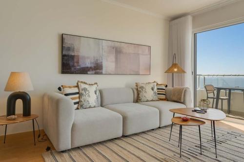 ein Wohnzimmer mit weißem Sofa und großem Fenster in der Unterkunft Sunflower Ocean View Apartment With Pool & Parking in Caniço
