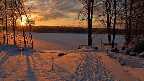 una puesta de sol invernal sobre un lago con huellas en la nieve en Dworek Hołny, en Hołny Wolmera
