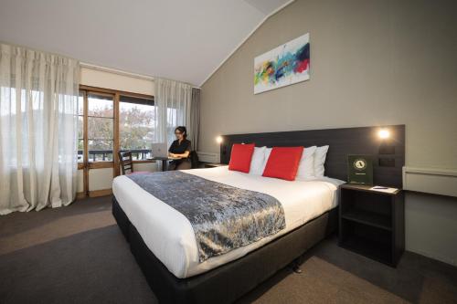 a hotel room with a bed and a woman sitting in a chair at Carnmore Hotel Lower Hutt in Lower Hutt