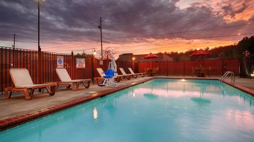 a swimming pool with chairs and a sunset in the background at Best Western Plus Gadsden Hotel & Suites in Gadsden