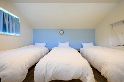 three beds in a room with white sheets at Aoshima Surfers House in Miyazaki