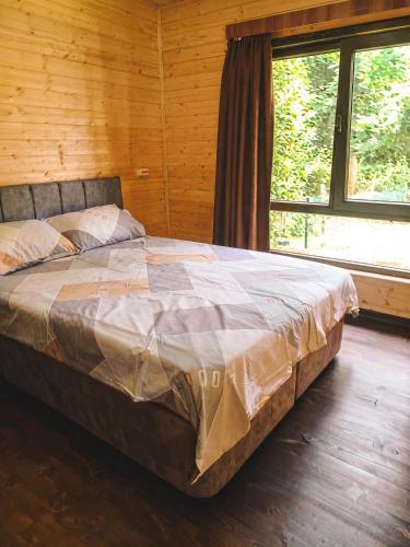 a bed in a wooden room with a large window at Shekvetili Cottage Nene in Shekhvetili