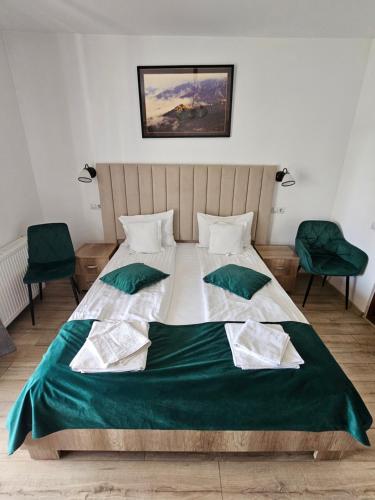 a bedroom with a large bed with two green chairs at Pensiunea Nobila Băile Figa in Beclean
