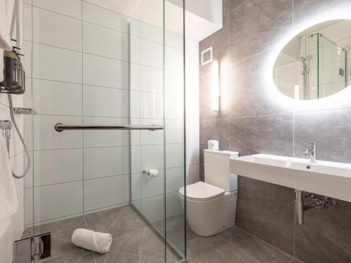 a bathroom with a sink and a toilet and a mirror at Auckland Rose Park Hotel in Auckland
