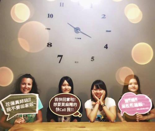 three women holding signs in front of a wall with a clock at Bayhouse Comfortel Hualien Hostel in Hualien City