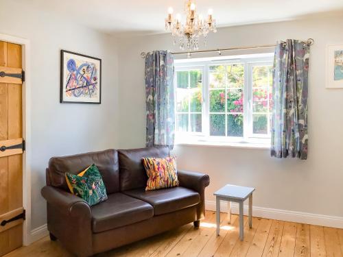 a living room with a leather couch and a window at Woodbrook Cottage in Bridport